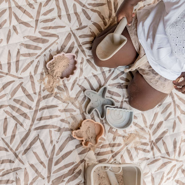 Overhead view of sand toys and child on textured mat surface – toddlekind portable water resistant wander classic play mat ocean tan with easy-clean material
