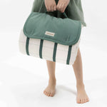 Child holding folded striped play mat with green flap and handle – toddlekind portable water resistant wander grande play mat forest for easy carrying
