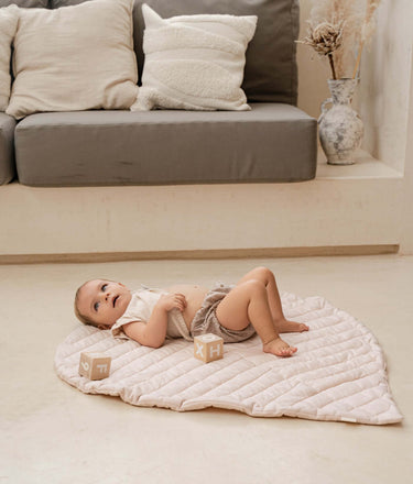 Baby lying and relaxing on organic cotton padded baby toddler play mat tummy time toddlekind quilted leaf mat blush in a cozy home setting.
