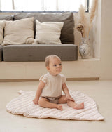 Baby sitting on organic cotton padded baby toddler toddlekind play mat tummy time quilted leaf mat blush in a soft neutral living room.
