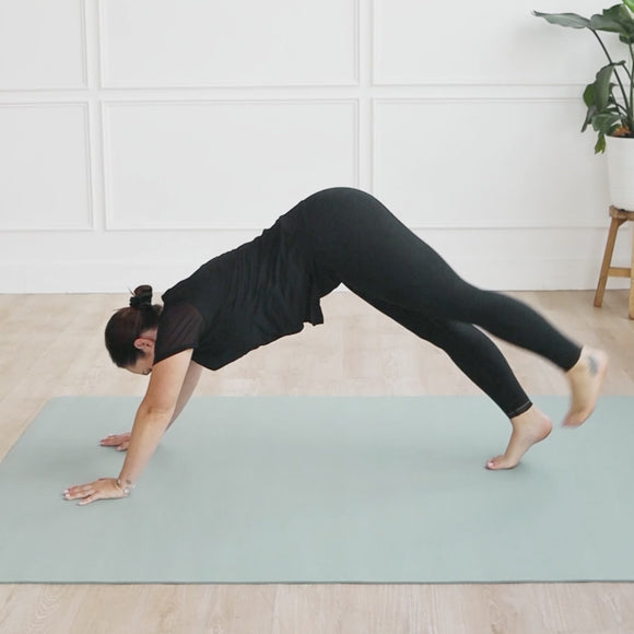 Person practicing yoga on an Evo Mat in sage color, demonstrating a downward dog position.