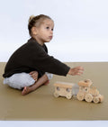 Toddler playing with wooden train while seated on toddlekind baby toddler foam modern puzzle play mat classic sandstone in minimal space.
